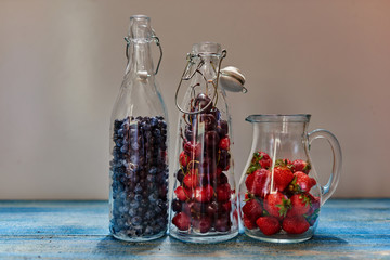On the vintage wooden table, there are three glass carafe which are prepared fresh berries for...