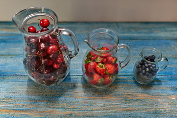 On the vintage wooden table, there are three glass carafe which are prepared fresh berries for...