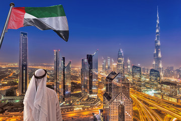 Arabischer Mann, der das Nachtstadtbild von Dubai mit moderner futuristischer Architektur in den Vereinigten Arabischen Emiraten beobachtet