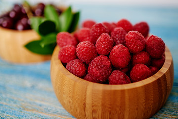 Bowl with red fresh raspberries on blue rustic wood table. Fresh garden raspberries in wooden bowl. Healthy breakfast concept. Selective focus.