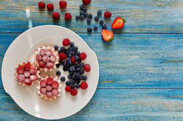 Party food. Mini cakes with berry mousse, caramel and fresh berries. Fresh homemade tarts with blueberry and cream  cheese on plate on the rustic wooden background. Top view. Selective focus..