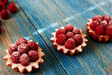 Delicious mini tarts made of oatmeal with fresh raspberries and custard on a wooden blue table. A homemade dessert made from delicious mini cakes. Healthy snack. Useful breakfast. Selective focus.