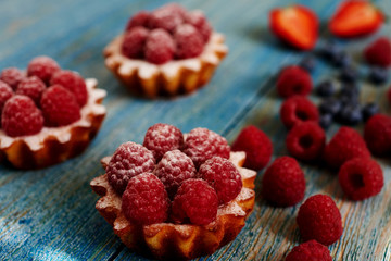Delicious mini tarts made of oatmeal with fresh raspberries and custard on a wooden blue table. A homemade dessert made from delicious mini cakes. Healthy snack. Useful breakfast. Selective focus.