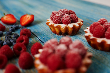 Close-up on a blue wooden kitchen table are just baked tartlets on top of fresh raspberries