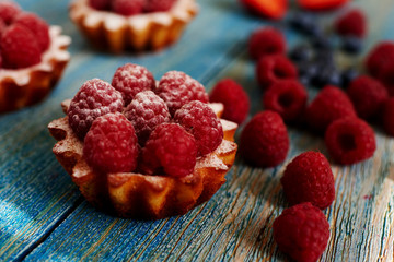 Delicious mini tarts made of oatmeal with fresh raspberries and custard on a wooden blue table. A homemade dessert made from delicious mini cakes. Healthy snack. Useful breakfast. Selective focus.