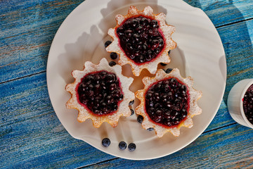 Bright and tasty dessert is on the kitchen table, vintage, tartlets with jam neatly on a white circular plate, is seen next to a small bowl with the remaining home-made jam from