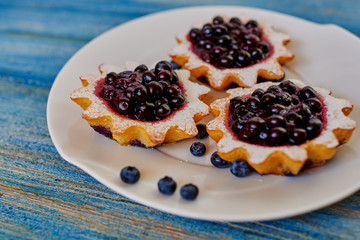 A delicious sweet dessert stands in the kitchen in a trendy coffee shop, cook gently served on a plate of light dough tartlets with berry jam