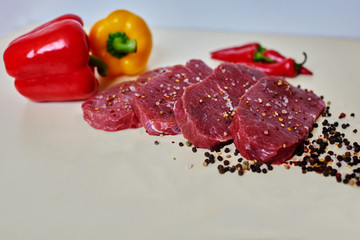 On a white kitchen table in the steakhouse cook beef tenderloin cut into portions small steaks, lie near large fresh peppers, it fry them on the grill and served as a side dish