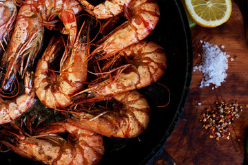 Roasted tiger prawns on a hot cast iron  fried in butter with lime and herbs in the restaurant. Process of cooking. Shrimp on the grill.  Exquisite dish of seafood. Food background. Selective focus.