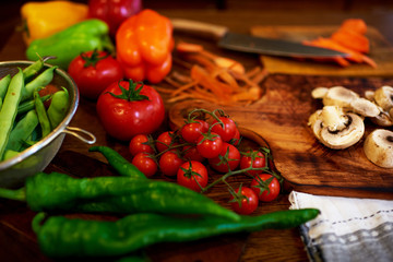 Tomatoes, red peppers, chili pepper lie on a chopping board, a knife lying nearby, in an aluminum bowl are just washed peas