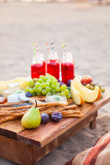Picnic on the beach at sunset in the style of boho. Concept outdoors evening healthy dinnner with fruit and juice