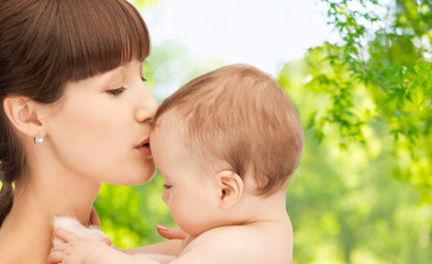 family and motherhood concept - happy smiling young mother kissing little baby over green natural...