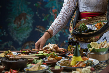 Indonesian cuisine - Many traditional Balinese dishes on the table. Waitress is serving food for some festive event, party or wedding