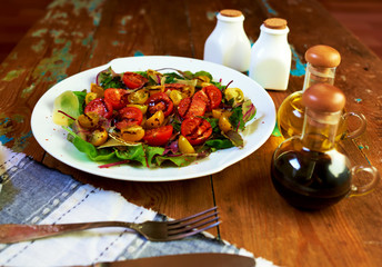 On the table is a stylish vintage dish with a salad of fresh leaves, arugula and cheese salad dressed with balsamic vinegar and olive oil, silver cutlery lie close