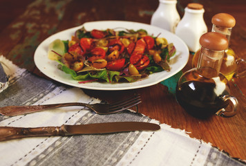 On the table is a stylish vintage dish with a salad of fresh leaves, arugula and cheese salad dressed with balsamic vinegar and olive oil