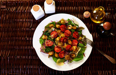 Light healthy salad of cherry tomatoes of different greens and parmesan cheese, salad served in a stylish deep white plate beside lie on linen napkin silver cutlery