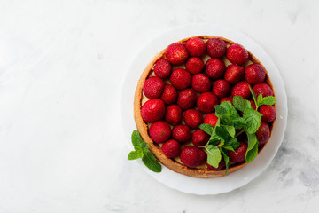 Cheesecake with fresh strawberries and mint on white plate on gray concrete background. Top view.