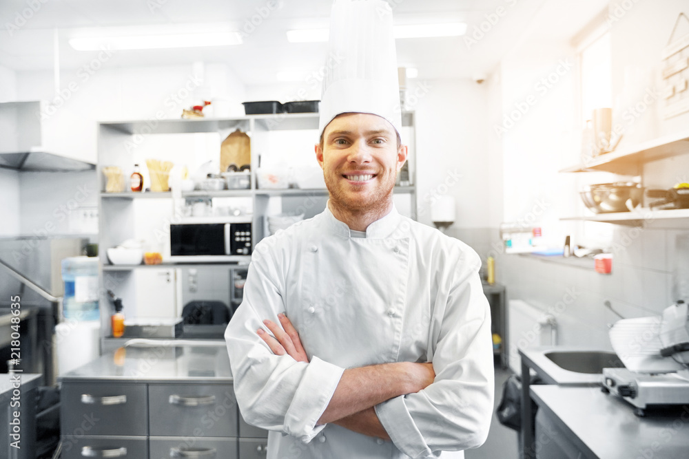 Wall mural cooking, profession and people concept - happy male chef cook  in toque with crossed hands at restaurant kitchen