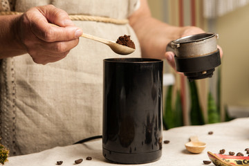 Women's hands putting some ground coffee from black coffee-grinder into holder. Close up.