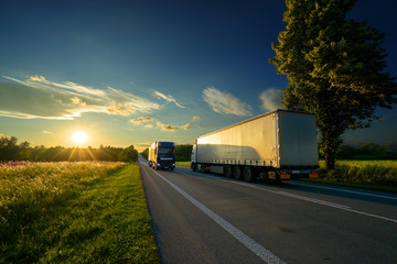 Trucks driving against each other on an asphalt road in a rural landscape at a golden sunset
