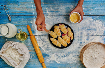 Fototapeta premium Female hands smeared with egg cakes before you put it in the oven to bake, which lies next to a rolling pin rolling out dough for roguelike