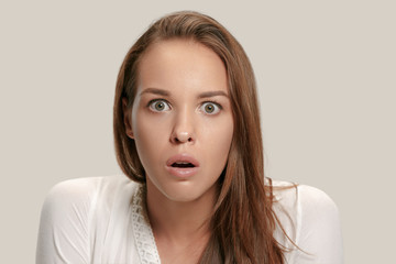 Wow. Beautiful female half-length front portrait isolated on gray studio backgroud. Young emotional surprised woman standing with open mouth. Human emotions, facial expression concept.