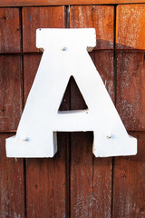 Big white letter A on dark wood background illuminated by the sun