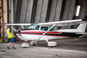 Single engine aircraft, ultra light plane ready for flight. Pilot is pulling out small motor air plane out from hangar in an old airport. Private airport, pilot school. Learning to fly in sunny day