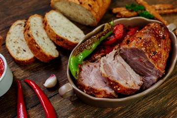 Baked sliced pork loin in ceramic form with fork, knife and homemade rustic bread on dark rustic background. Roasted pork served with grilled vegetables and tomato sauce. Cozy village dinner..