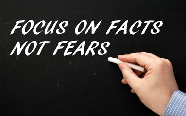 Hand writing the words Focus on Facts Not Fears on a blackboard in white text as a motivational message