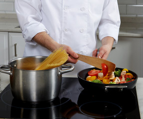 Cook man standing near the plate, cook pasta and puts vegetables and mushrooms in a skillet