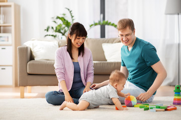 family, parenthood and people concept - happy mother, father and baby boy playing toy blocks at home