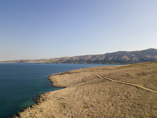 Vista aerea di una strada serpeggiante che costeggia dele coste della Croazia, strada non asfaltata, isola di Pag, spiaggia di Rucica a Metajna. Natura selvaggia ed incontaminata. Mare trasparente 