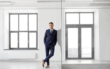 business and people concept - smiling businessman at office glass wall