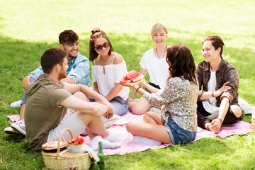 friendship, leisure and summer concept - group of happy friends eating watermelon at picnic in park