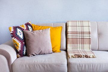 Cushions and plaid on the beige sofa close up with copy space. Sweet home and cozy concept