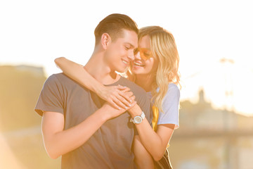 happy girlfriend hugging boyfriend on river beach during sunset