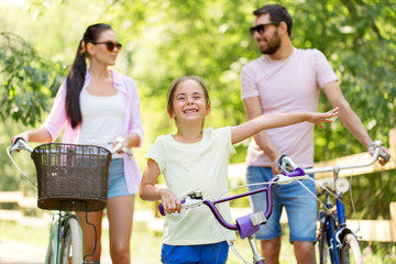 Obraz premium family, leisure and people concept - happy mother, father and little daughter with bicycles in summer park