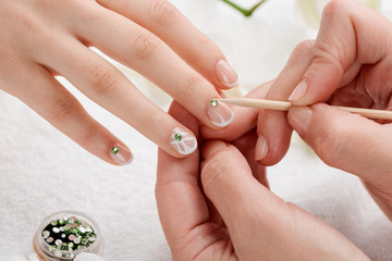 Beautician attaching green rhinestones on nails. Chic and fabulous design over French manicure base.