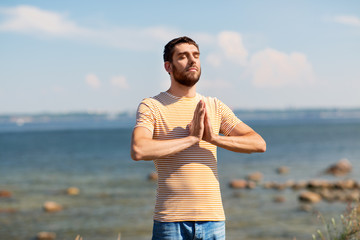 Fototapeta na wymiar meditation, spirituality and mindfulness concept - man meditating outdoors over sea