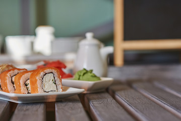 Rolls with salmon and cheese served ginger and wasabi. Delicious traditional japanese food on a  white porcelain plate  for sushi on wooden background. Sushi menu. Selective focus.