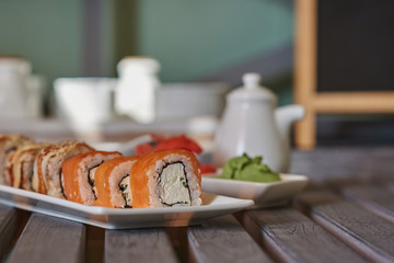 Rolls with salmon and cheese served ginger and wasabi. Delicious traditional japanese food on a  white porcelain plate  for sushi on wooden background. Sushi menu. Selective focus.