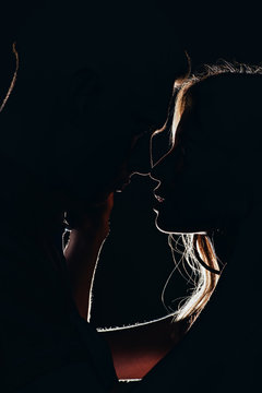 silhouettes of young tender couple going to kiss in dark