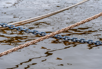One chain and three ropes with reflecting water surface in the background at daylight.