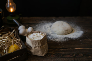 Baking ingredients placed on wooden table, ready for cooking. Concept of food preparation. Kitchen table with ingredients for cooking bread or pizza. Raw dough, flour, eggs on the wooden table.