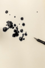 An overhead closeup photo of drops of ink and a nib pen, with copy space