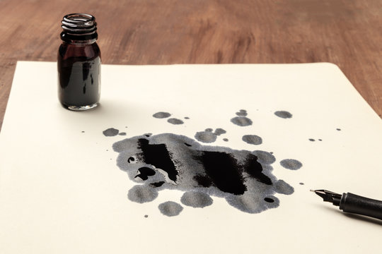 A photo of drops of ink on paper, an ink well and and a nib pen, with copy space