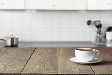 Cup of coffee on wooden board. Blurred kitchen as background.