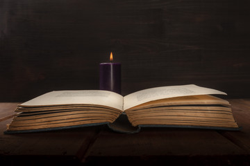 An open old book on a dark background with a burning candle and copy space