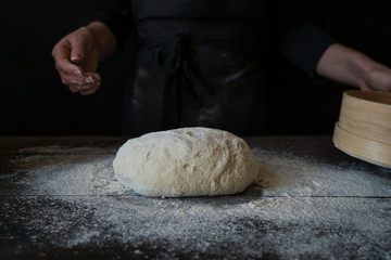 Food, cooking and baking concept. Yeast bread dough rising on wooden kitchen table at bakery. Woman preparing bread dough on wooden table in a bakery close up. Preparation of easter bread.